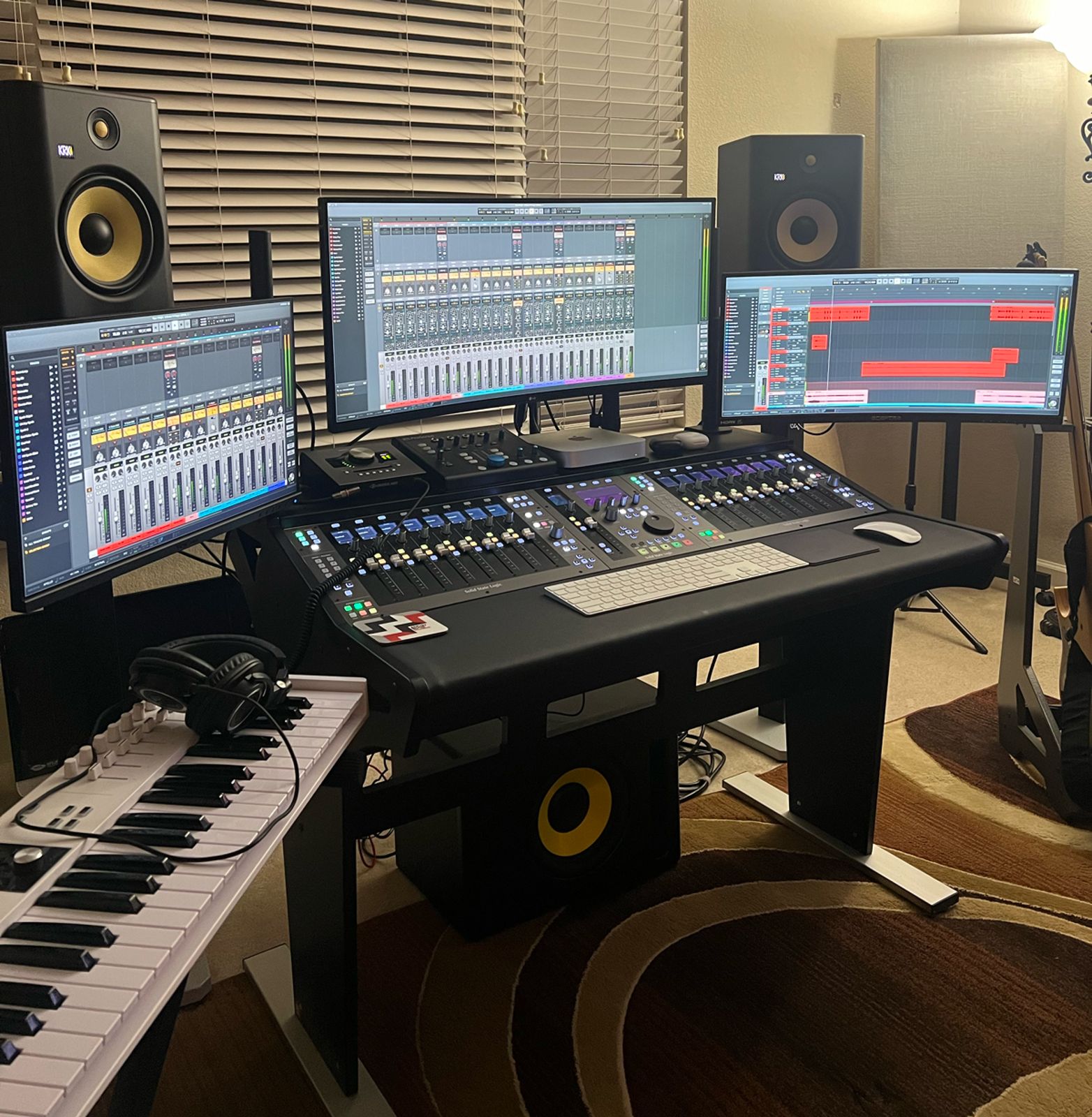 Music production setup with multiple monitors, a keyboard, and audio equipment.